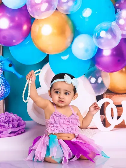 Holding a string of pearls, this little mermaid looks like true ocean royalty. The balloon arch adds a festive touch to the underwater scene.