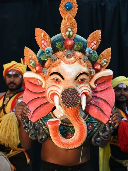 A large, ornate Ganesha mask from Nepal, showcased by traditional dancers. The vibrant colors and detailed design reflect the rich spirituality of the culture and are believed to ward off evil spirits.