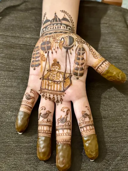 A sweet design for Janmashtami, featuring Bal Gopal (baby Krishna) in a cradle. The fingers are decorated with little birds, adding to the playful and divine theme.
