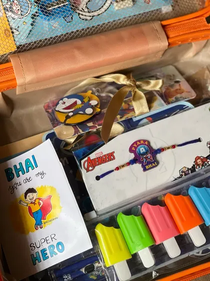 A close-up of the items packed in the kids' Rakhi hamper, including an Avengers Rakhi, a "Super Hero" card, and fun highlighters.