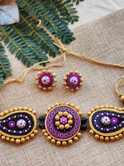 A statement terracotta choker necklace with paisley and circular motifs in purple and gold. This is a bold piece perfect for special occasions.