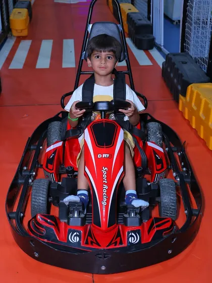 A front-on view of a young boy in a red go-kart, showcasing the cool "Sport Racing" design.