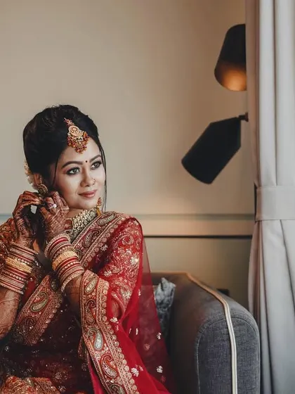 A candid getting-ready moment. The bride is captured adjusting her earring by a window, the natural light creating a soft and intimate feel.