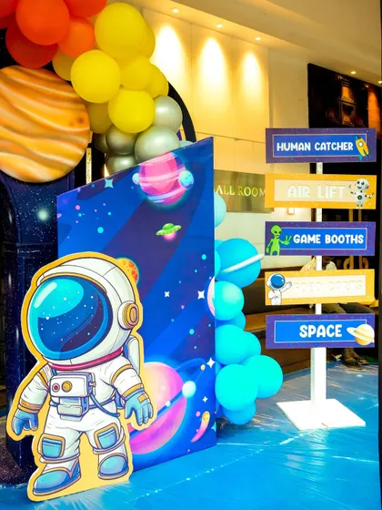 Themed decor for a space party, including an astronaut cutout and a directional sign pointing to activities like 'Human Catcher' and 'Game Booths'.