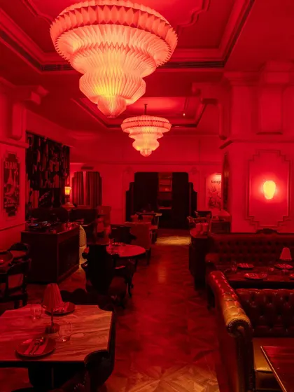 The interior of BANNG restaurant, bathed in an intense, monochromatic red light. This immersive color choice creates a powerful and theatrical atmosphere, punctuated by ornate chandeliers and classic furniture silhouettes.