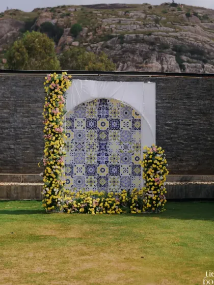 A modern and artistic Haldi backdrop, featuring a mosaic of blue and yellow tiles framed by an arch of yellow flowers.