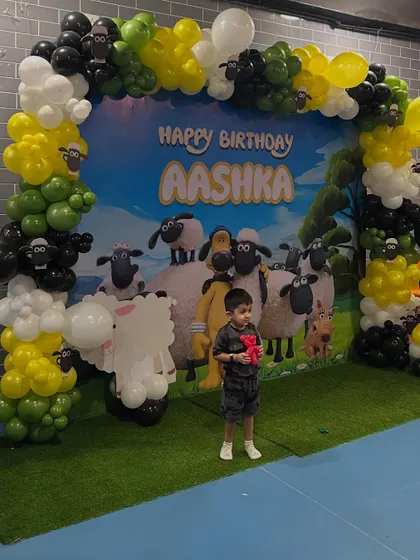 A unique Shaun the Sheep themed birthday party. This creative setup features a custom backdrop of the farm, with a balloon arch in green, yellow, black, and white to match the characters.