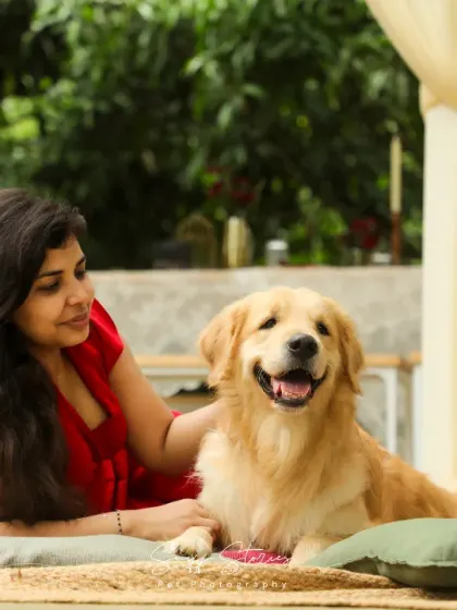 A woman in a red dress shares a happy moment with her Golden Retriever, relaxing together on a patio in a beautiful Bangalore setting.
