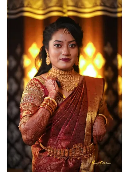 A beautiful bridal portrait against a warm, glowing background, showcasing her intricate red and gold saree.