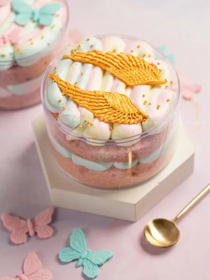 A whimsical Vanilla and White Chocolate Mousse Cake Tub, decorated with pastel marshmallows and golden angel wings. It's a dessert straight out of a fairy tale.