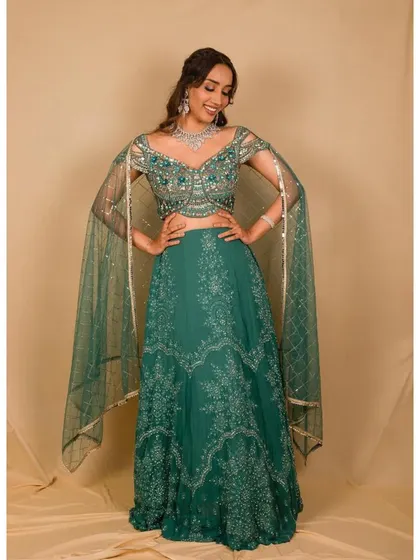 This elegant teal green lehenga features delicate silver embroidery and unique, flowing cape-style sleeves. It's a sophisticated and modern take on the traditional lehenga, perfect for a wedding guest.