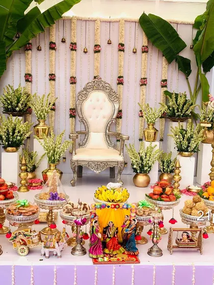 An elegant and classic Seemantham setup featuring a silver throne, fresh jasmine and tuberose flower arrangements, and large banana plants for an authentic traditional feel. The foreground is filled with auspicious items and doll displays.