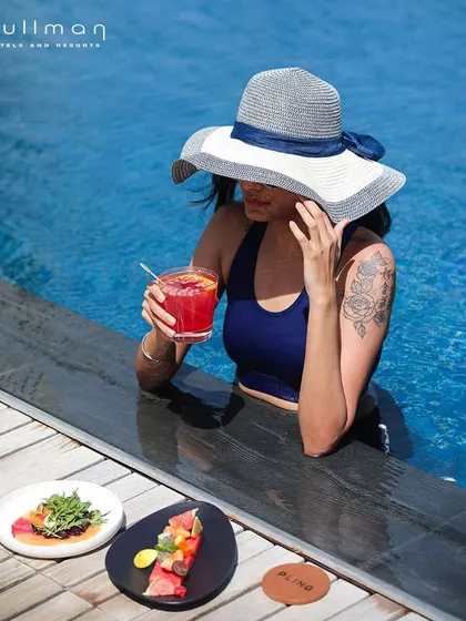 A woman relaxes in the Pullman hotel pool with a cocktail and snacks. This image perfectly blends luxury, relaxation, and indulgence for a perfect afternoon.