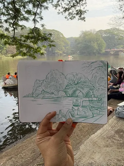 There is a special connection formed when you draw a place while you are in it. I held up my finished sketchbook to show my pen drawing against the real boating lake at Sanjay Gandhi National Park. My goal is to capture the essence of the scene, not just a perfect copy.