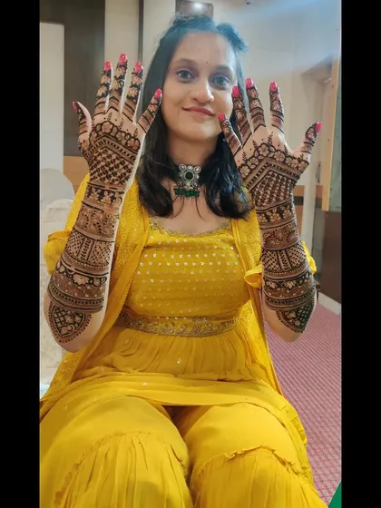 A happy client proudly showing both her hands, covered in a dense, traditional mehendi design that extends up to her elbows.