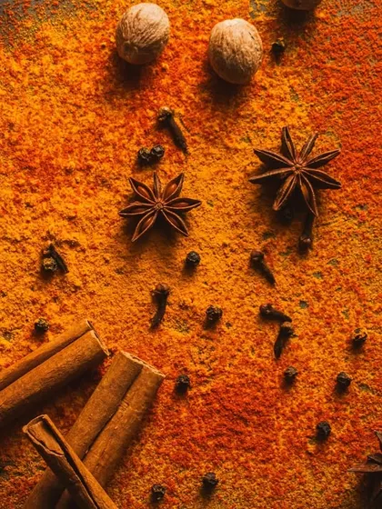 A close-up flat lay of spice powders and whole spices like star anise and cinnamon. The warm, intense lighting and dark background create a fiery and dramatic mood.