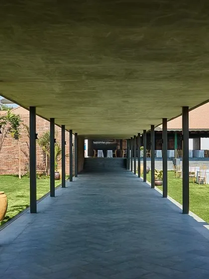 A long, covered walkway at Samavana, defined by a series of slender columns. This element provides shelter while maintaining an open connection to the lawn, guiding guests through the venue with a sense of rhythm and order.