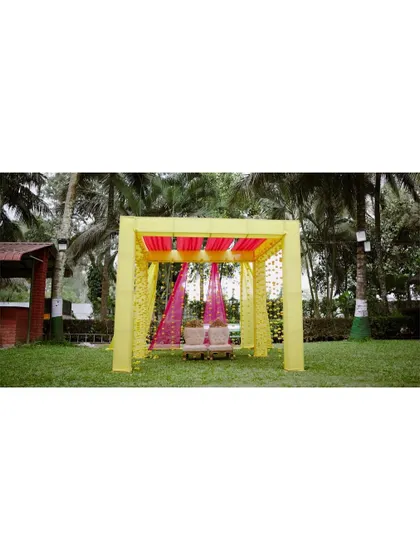 A duplicate of a wide shot of the beautiful outdoor setup for a Haldi ceremony, with a vibrant yellow and pink mandap.