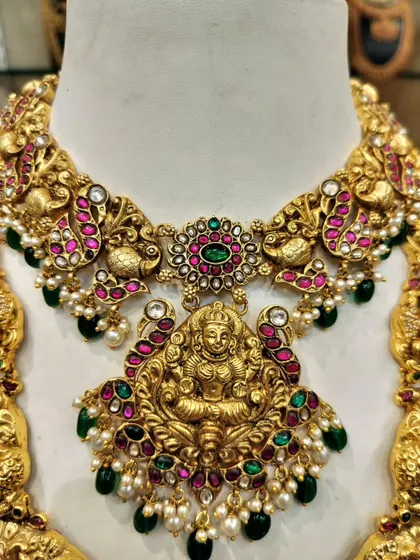 A close-up of a Lakshmi pendant, showcasing the detailed craftsmanship and the vibrant colors of the Kempu and green stones.
