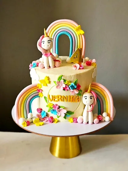 This unicorn-themed cake features two rainbows and two unicorn figurines, making it extra special. The design is adorned with small, colorful, handmade flowers and butterflies.