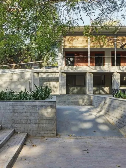The CEPT University Canteen is nestled between mature trees, with its structure carefully integrated into the existing landscape. The use of concrete steps and planters helps to merge the building with its site.