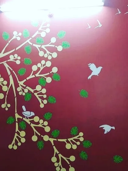 A completed nature mural on a bold red wall. The contrast between the red background and the white and green tree design makes for a vibrant feature wall.