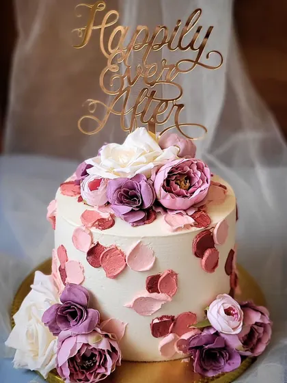 A beautiful engagement cake with palette-knife buttercream swatches in shades of pink and purple. The "Happily Ever After" topper and fresh flowers complete this romantic design.