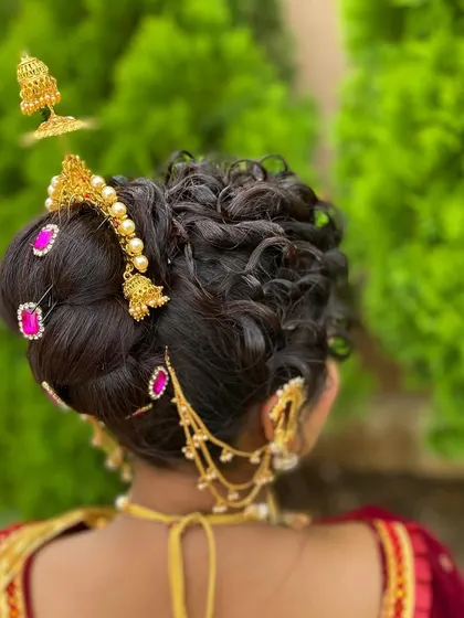 The back view of a traditional bridal updo. This style showcases intricate curls and the placement of classic temple jewelry, including jhumkas and hairpins, for a complete ceremonial look.