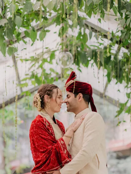 An intimate, close-up portrait of Kayla and Tushar, their faces close together, framed by the lush greenery of their wedding venue.