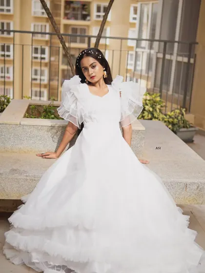 This fairytale white gown features dramatic ruffled sleeves and a tiered skirt. It's a perfect choice for a bride who wants a high-fashion, ethereal look for her special day.