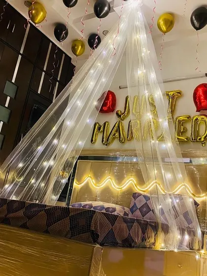The 'Just Married' setup with gold and black balloons. The fairy lights on the canopy and headboard create a warm and inviting glow.