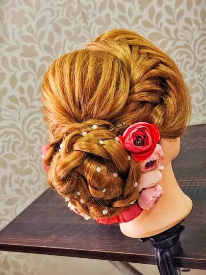 A beautiful braided bun accented with pink roses and pearls, created by a student during practice.