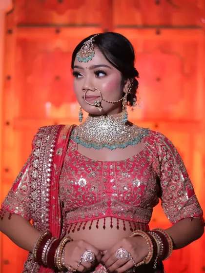 A medium shot of the bride against a red-lit heritage door. This photo captures her looking away, highlighting her profile, makeup, and the detailed embroidery on her blouse.