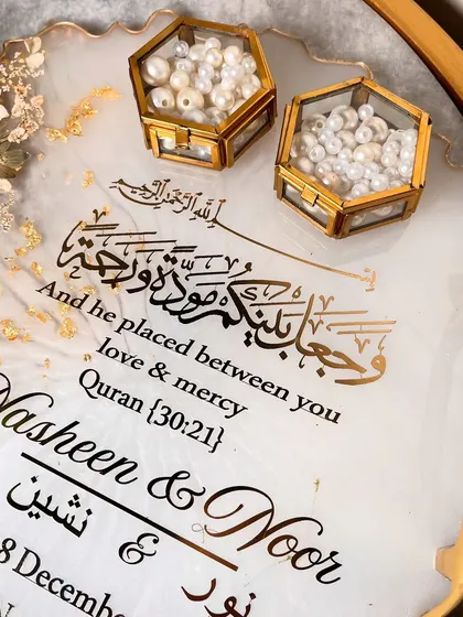 An elegant white and gold ring tray with delicate daisy-like flowers and a beautiful Quranic verse. The hexagonal ring boxes are filled with pearls.