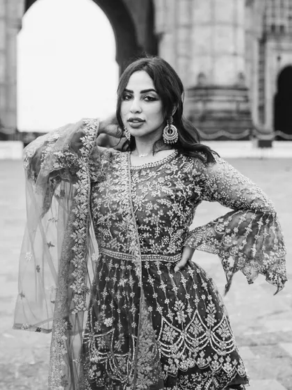 A close-up portrait in black and white, focusing on her confident pose and the intricate details of her attire and jewelry.