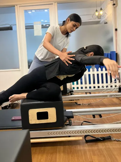 An instructor provides guidance on a back extension exercise on the reformer box during our teacher training program.