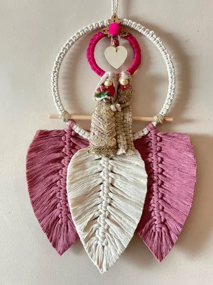 A perfect gift for a wedding or anniversary. This custom piece features adorable couple dolls set within a macrame hoop, framed by two large feathers in pink and white.