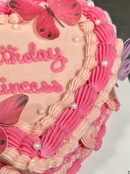 The detailed piping work on the side of the pink heart-shaped butterfly cake.