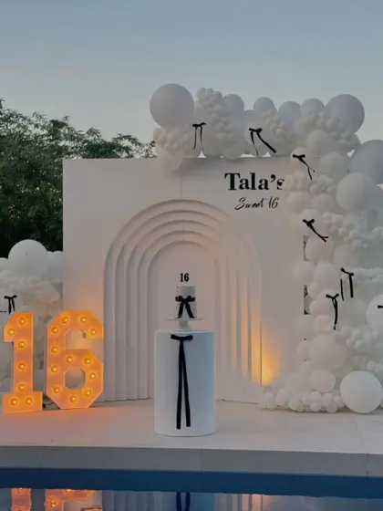 The sweet 16 setup with the marquee number '16' lit up as dusk approaches, adding a warm glow to the poolside celebration.