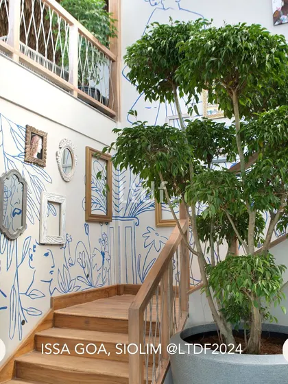 The staircase at ISSA Goa is a canvas for local art, with whimsical line drawings and curated frames creating a gallery-like experience. A large potted tree brings nature indoors, reinforcing the connection between the design and its lush surroundings.