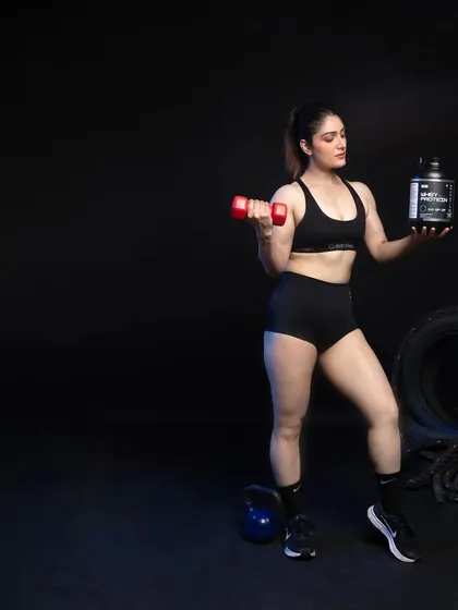 A female model holding a dumbbell and a whey protein container, showcasing both the action and the product in a single frame.