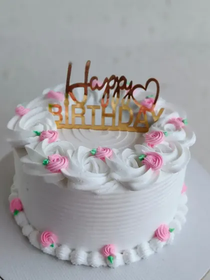 A classic birthday cake with white frosting and delicate pink piped roses.