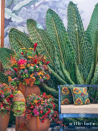 A detail of the Pellikuthuru ceremony decor, with a traditional mask and vibrant flowers set against the woven leaf backdrop.