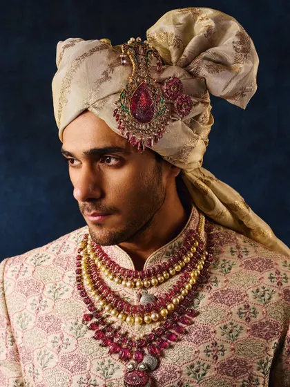 A portrait of a groom adorned in royal jewellery. The lighting is focused to bring out the rich red of the rubies and the texture of the brocade sherwani and turban.