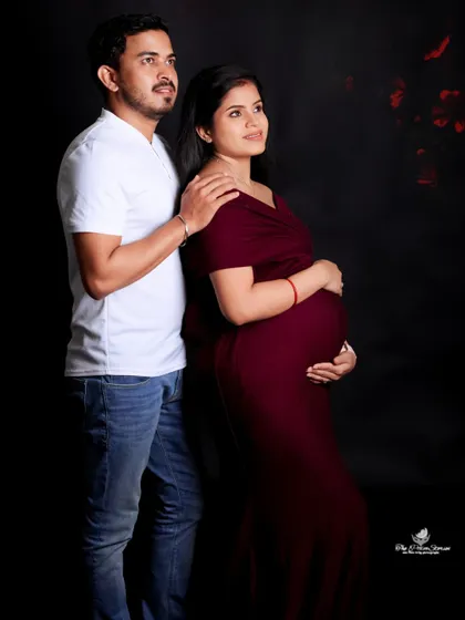 A simple and classic couple's portrait against a solid black background. The focus is entirely on their connection and the beautiful silhouette of the baby bump.