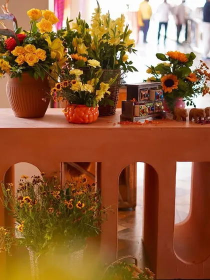 A modern terracotta-colored console table with arched cutouts, decorated with vases of yellow flowers and other small, traditional artifacts, showcasing our custom production capabilities.