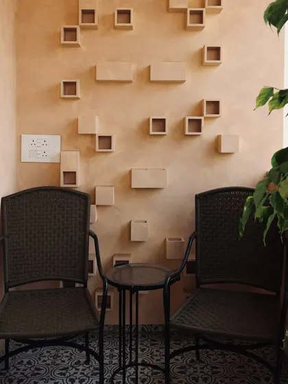 A cozy balcony corner designed for quiet moments. The textured wall with sculptural niches, patterned floor tiles, and woven chairs create a space that is rich in detail and character.