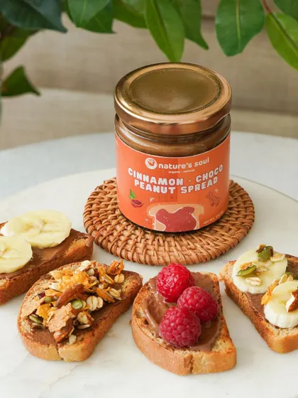 Showcasing the versatility of a cinnamon choco peanut spread with various toppings like banana, raspberries, and granola on toast.