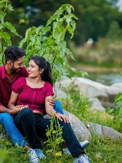 A relaxed and happy portrait of a couple sitting by the lake, framed by lush greenery.