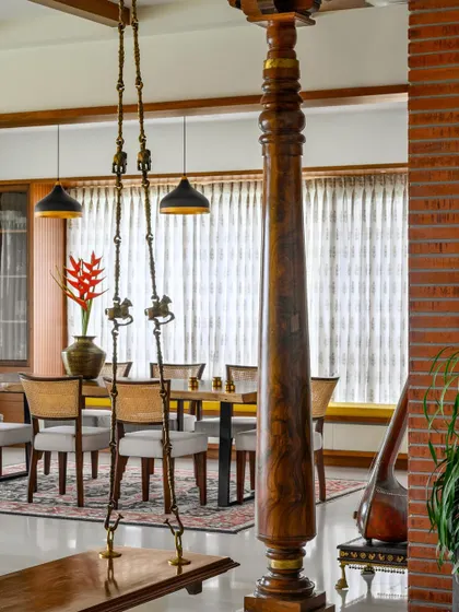 An introductory shot of 'Vasudhalayah', where a traditional swing and an antique Chettinad pillar frame the view into the dining area, showcasing the home's fusion of South Indian charm and modern design.